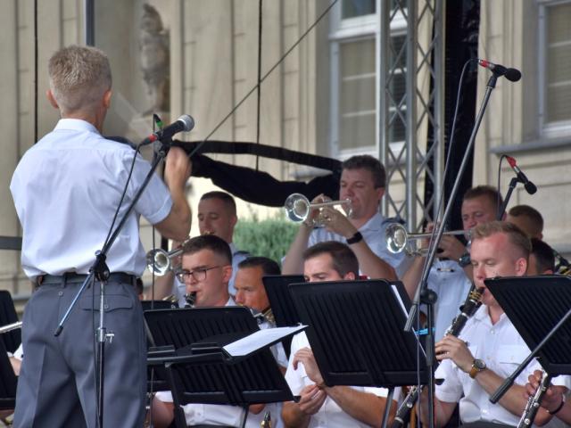 Dyrygent mjr Paweł Joks dyryguje orkiestrą, soliści-muzycy grają na trąbkach