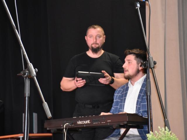 Instruktor Rafał Grygiel gra na pianinie, Wojciech Białasik czuwa nad właściwym nagłośnieniem